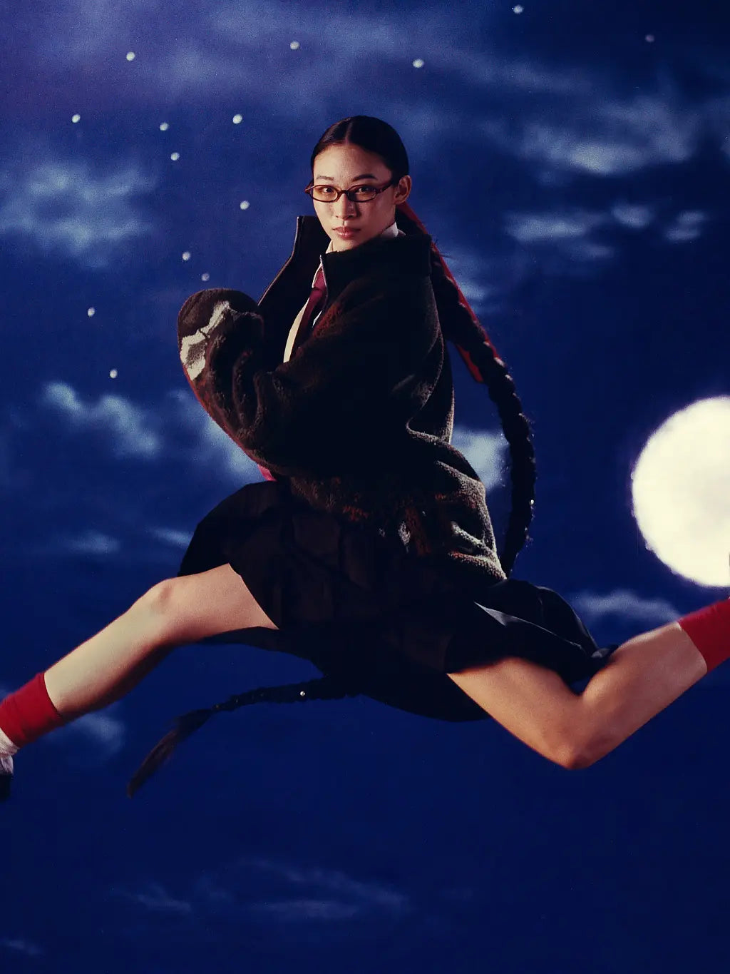 A person in Sundae School Five Peaks Fleece and skirt with red socks and glasses is posed mid-air against a night sky background with stars and a full moon.