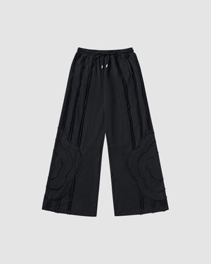 Black Mochi Haze Paneled Sweatpants featuring garment washed black cotton with exposed curved seam details throughout legs, elastic waistband with drawstring ties, relaxed wide-leg fit silhouette, flat lay product shot on light background.
