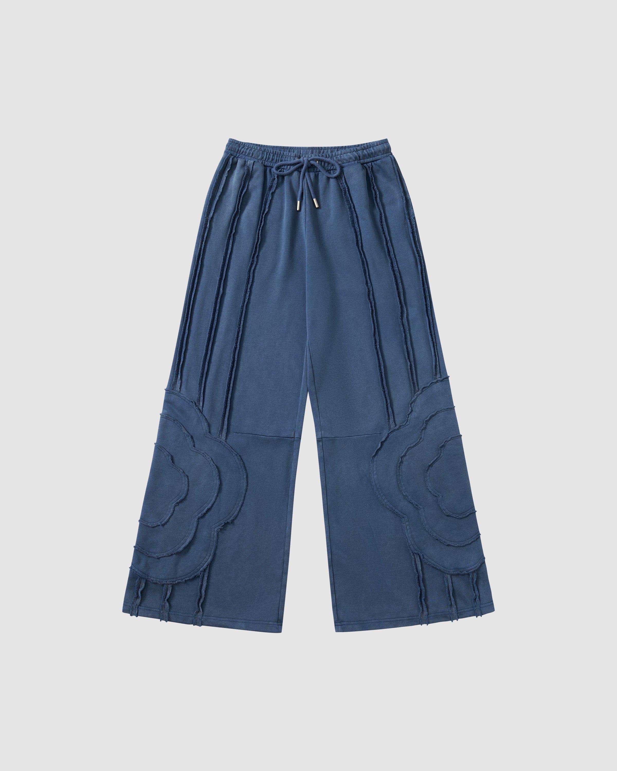 Indigo Mochi Haze Paneled Sweatpants featuring garment washed cotton with exposed curved seam details throughout legs, elastic waistband with drawstring ties, relaxed wide-leg fit silhouette, flat lay product shot on light background.