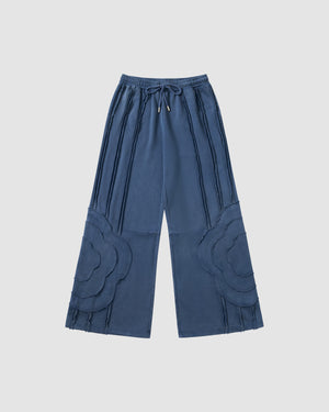Indigo Mochi Haze Paneled Sweatpants featuring garment washed cotton with exposed curved seam details throughout legs, elastic waistband with drawstring ties, relaxed wide-leg fit silhouette, flat lay product shot on light background.