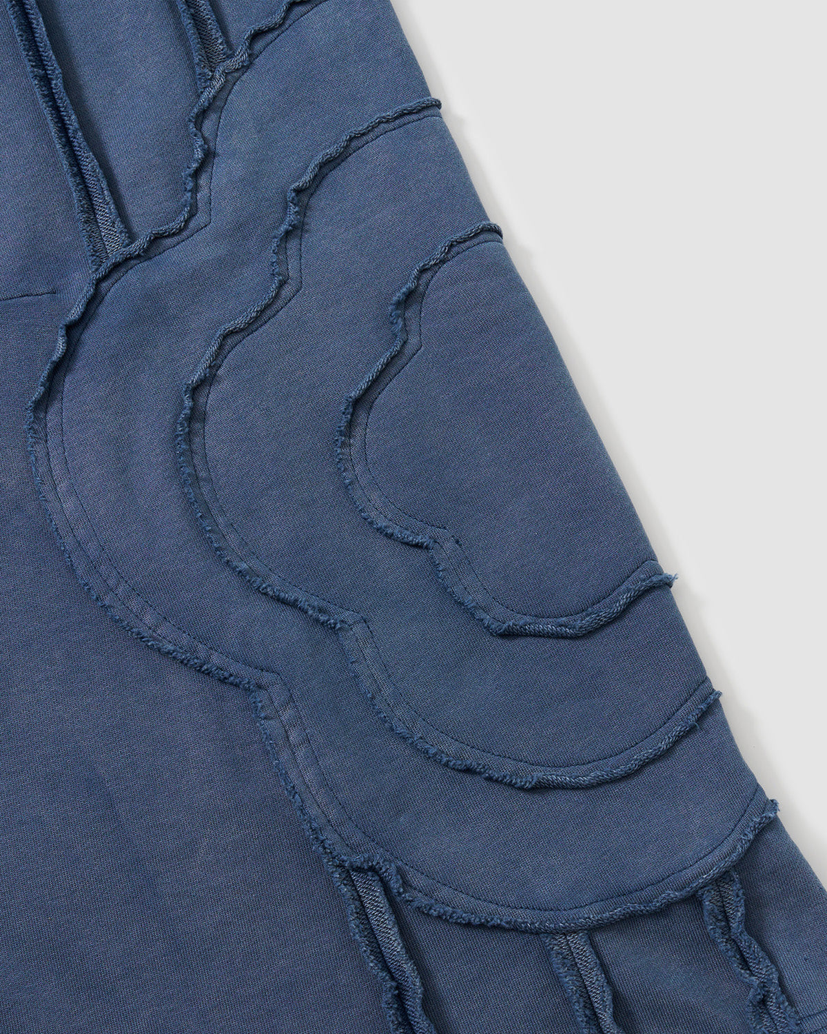 Indigo Mochi Haze Paneled Sweatpants close-up detail showing large curved exposed seam construction with flower-like pattern and frayed edges on garment washed indigo cotton fabric.