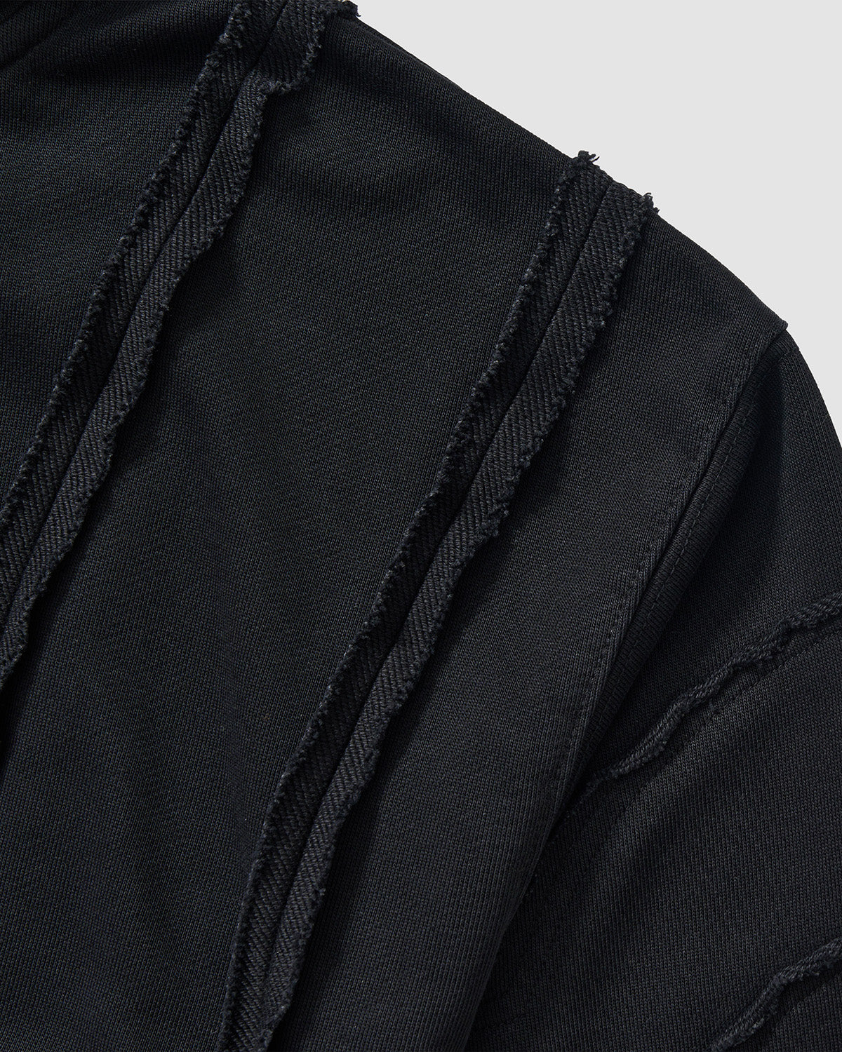 Black Mochi Haze Paneled Hoodie shoulder and chest area detail showing exposed curved seam construction with frayed edges, garment washed black cotton texture, and distressed finishing on light background.