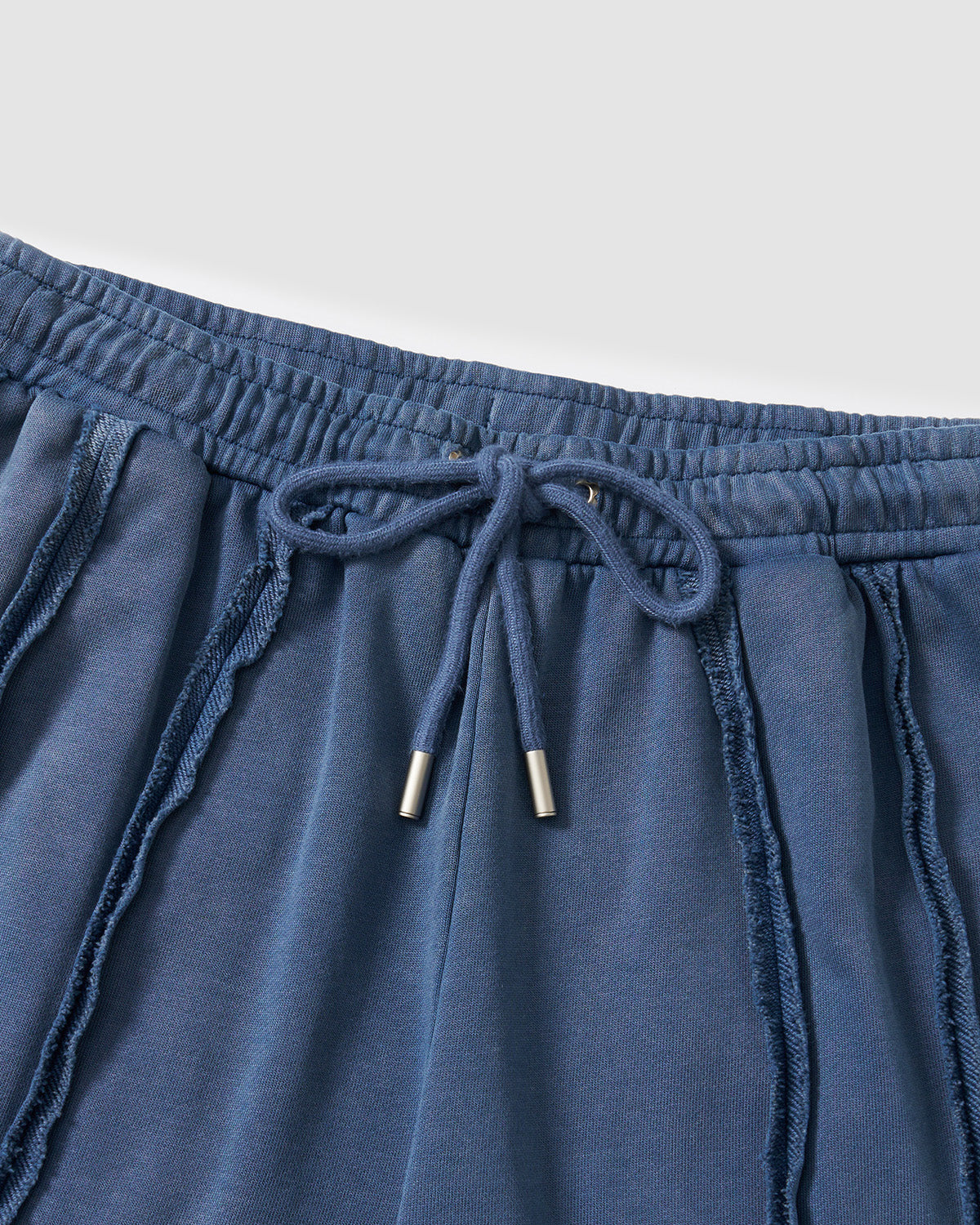 Indigo Mochi Haze Paneled Sweatpants close-up detail showing waistband area with exposed vertical seam construction and garment washed indigo cotton texture, flat lay on light background.