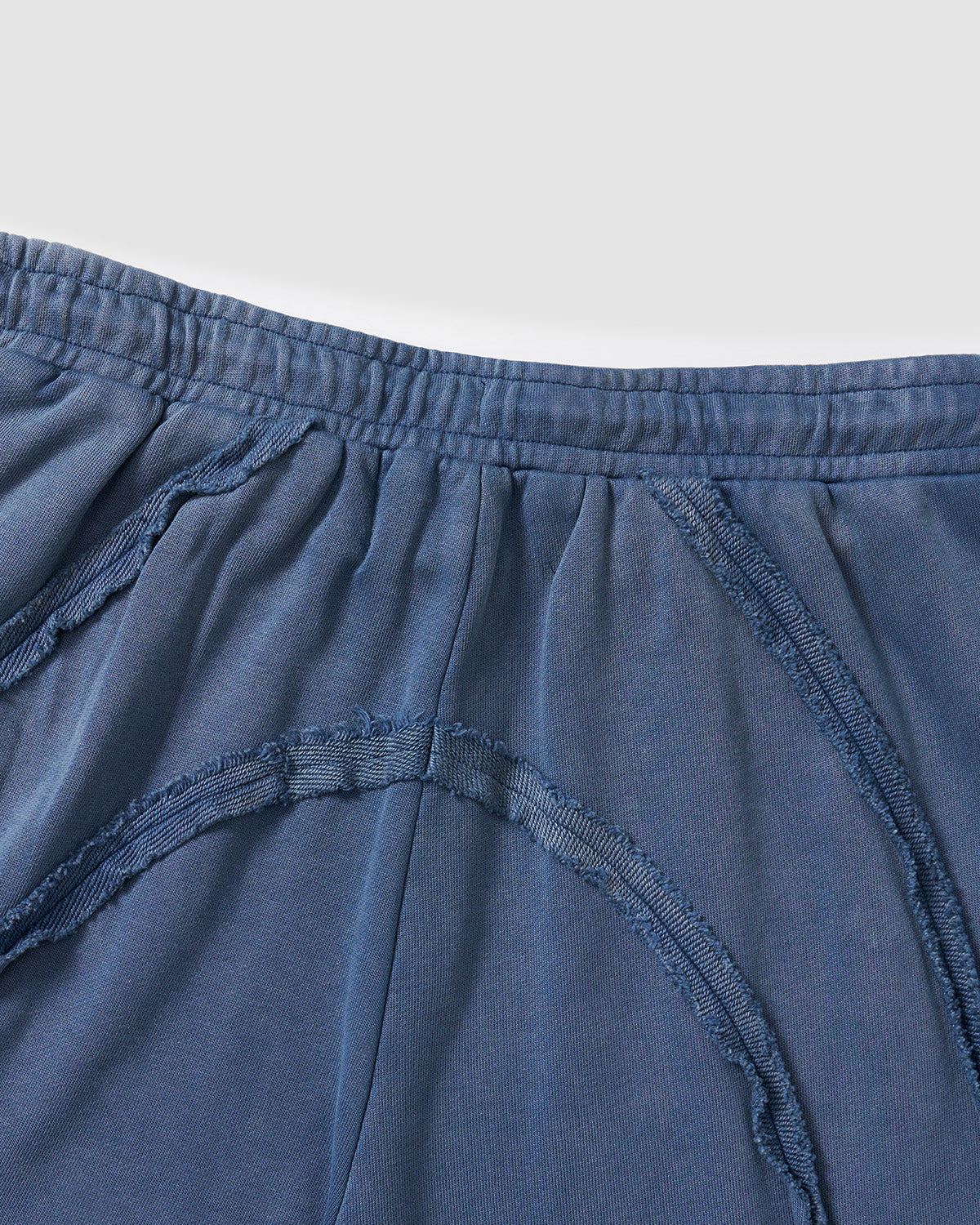 Indigo Mochi Haze Paneled Sweatpants close-up detail showing waistband area with exposed vertical seam construction and garment washed indigo cotton texture, flat lay on light background.