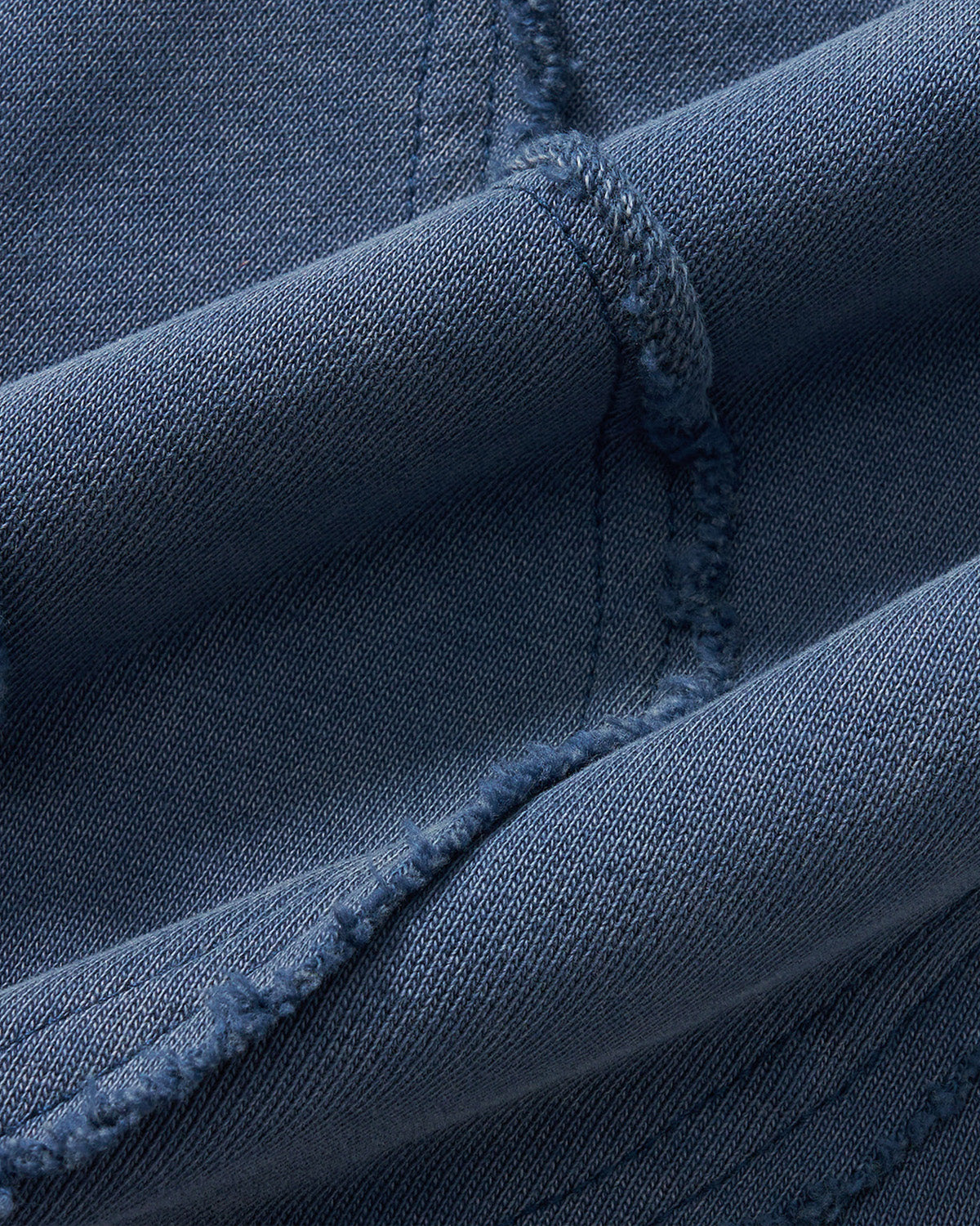 Indigo Mochi Haze Paneled Sweatpants fabric texture detail showing garment washed indigo cotton material with exposed seam construction and distressed finishing, close-up macro shot.