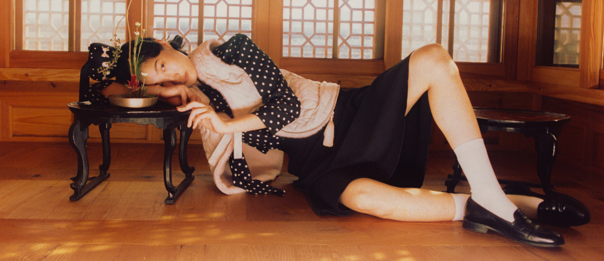 A girl wearing Sundae School Silver Pink Baeja Fur Trimmed Vest / Tote and lying on a small black table staring into the camera