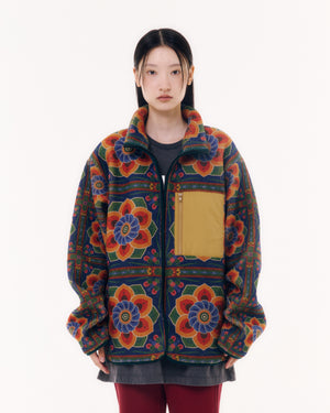 Sundae School Dancheong Fleece modeled front view on person with black hair, styled with dark gray dress and burgundy pants, showing vibrant Korean temple pattern and tan chest pocket detail, white studio background.