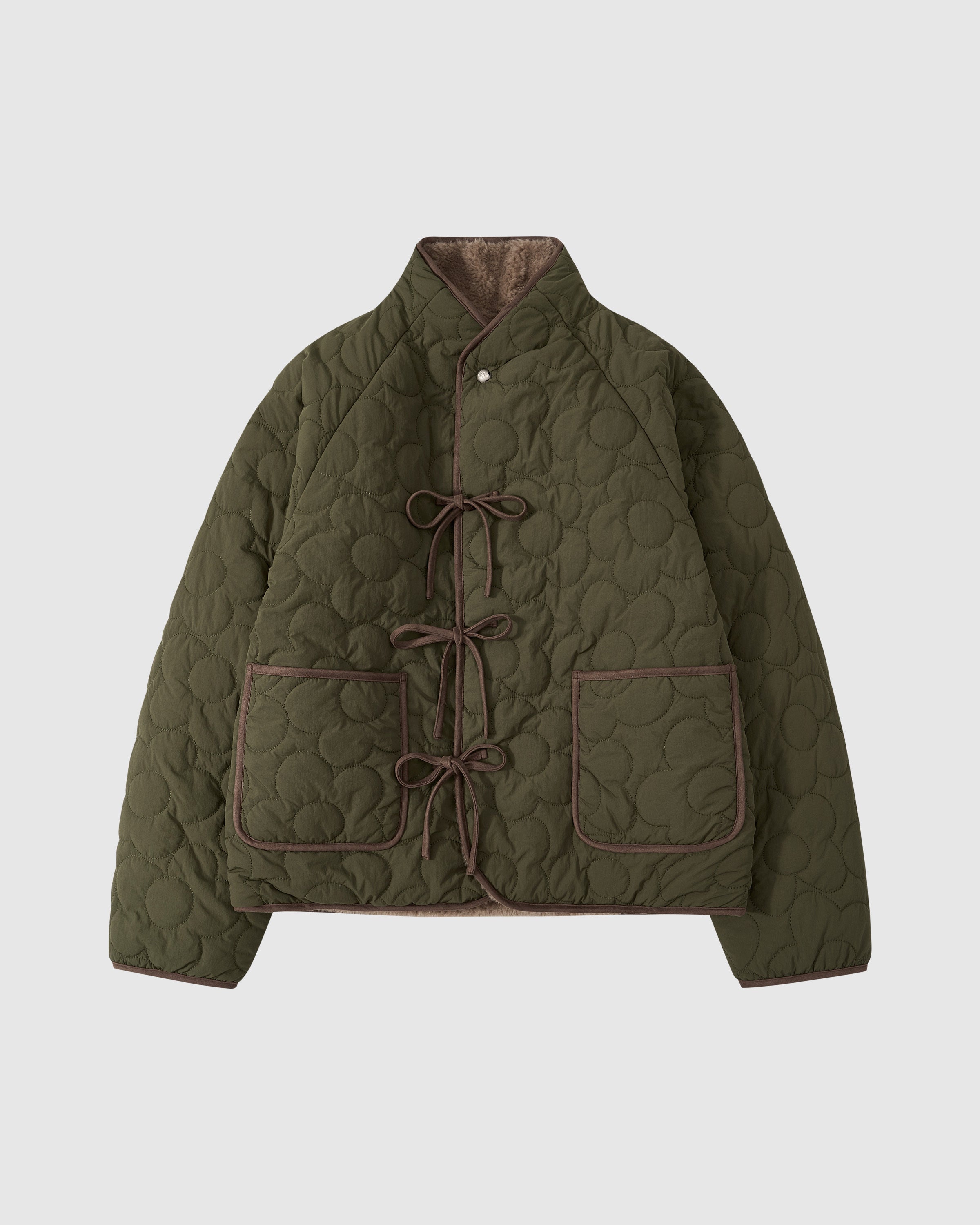 The REVERSIBLE FLOWER QUILTED JEOGORI FLEECE by Sundae School is an olive green hanbok-inspired jacket with brown trim, front ties, two large pockets, and a high collar, shown on a plain white background.