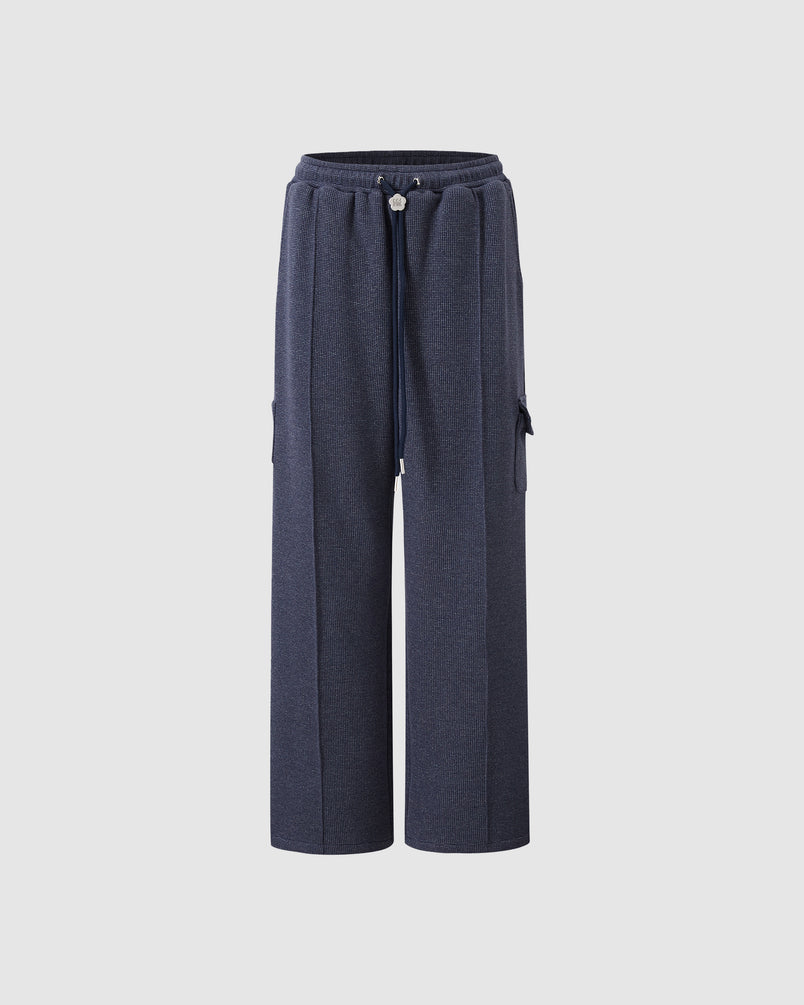 Sundae School navy waffle knit sweatpants featuring elastic waistband with drawstring closure, custom logo drawstring ends, side cargo pocket detail, wide-leg relaxed fit silhouette, waffle knit texture throughout, flat lay product shot on light background.