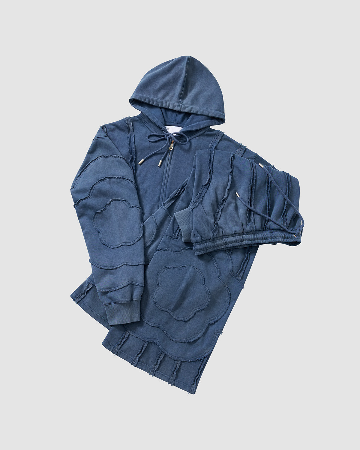 Indigo Mochi Haze Paneled Hoodie close-up detail shot showing garment washed indigo cotton texture, exposed curved seam construction, and fabric draping, flat lay on light background.