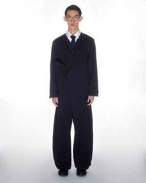 A person faces forward in a Sundae School NAVY HANBOK TIE BLAZER with an asymmetric side tie and wide-legged pants, paired with a white shirt and tie, set against a plain white background.
