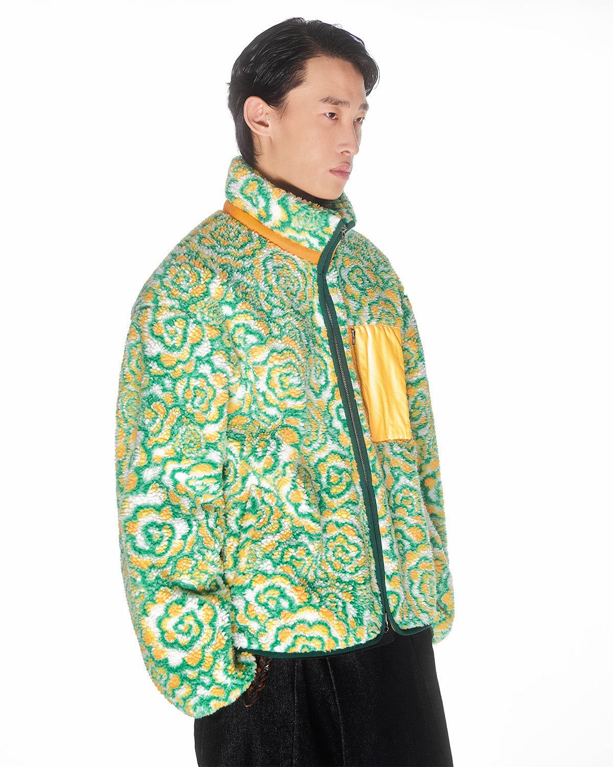 Someone wears the Sundae School Broccoli Fleece, a fluffy sherpa jacket in green, yellow, and white with a high collar, custom zipper, and shiny yellow chest pocket, standing against a plain white background.