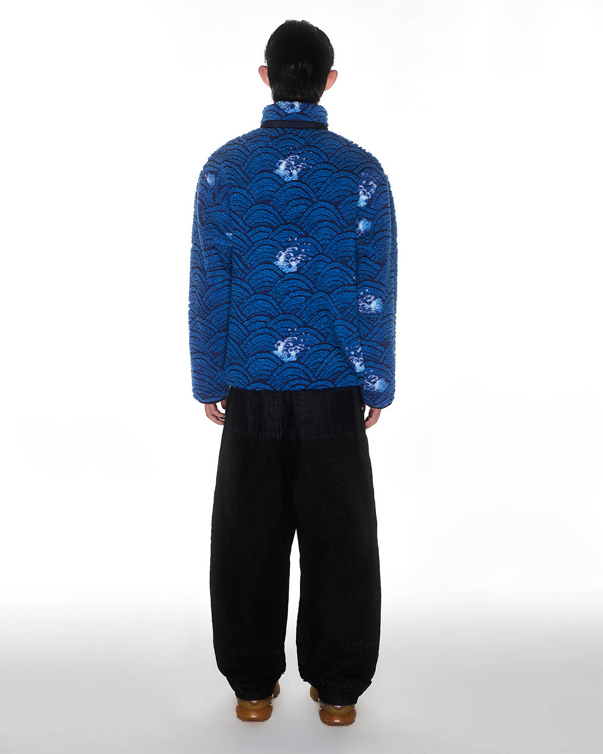 A person faces away, wearing the Sundae School BLUE WAVE FLEECE with wave and floral jacquard, paired with loose black pants and brown shoes, set against a plain white background.