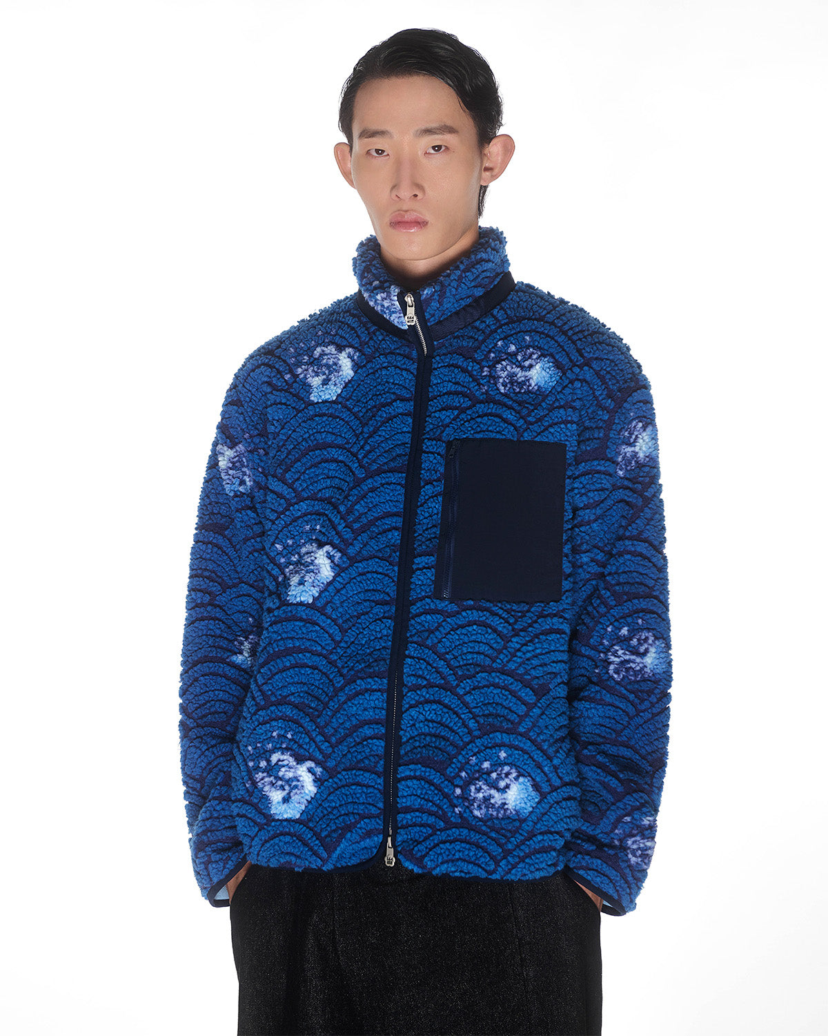 A person with short dark hair wears Sundae School's BLUE WAVE FLEECE, a blue embossed pile jacket with a custom wave jacquard and a dark blue chest pocket, standing against a plain white background.