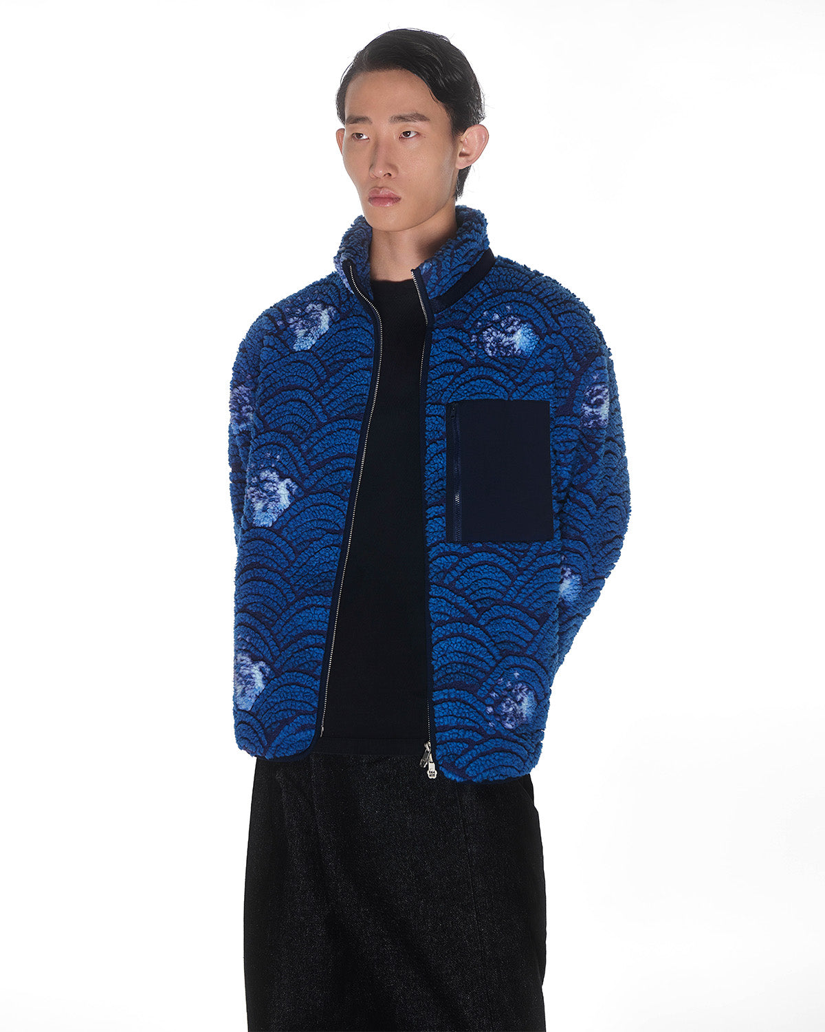 A person with long dark hair, wearing Sundae School's BLUE WAVE FLEECE over a black shirt, stands against a white background.