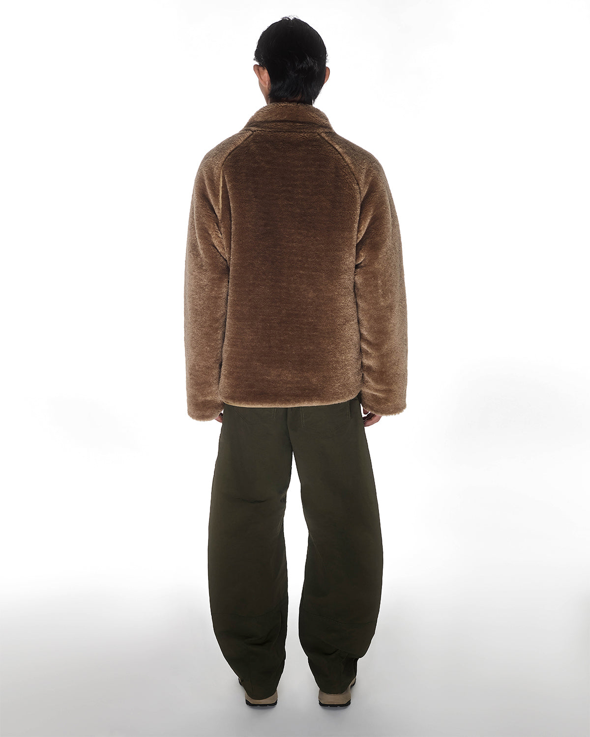 A person faces away from the camera wearing Sundae School’s [PRE-ORDER] REVERSIBLE FLOWER QUILTED JEOGORI FLEECE, paired with loose dark green pants and beige shoes, set against a plain white background.