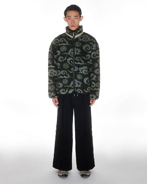 A person faces forward against a plain white background, wearing the Sundae School Kloud Fleece Zip-Up with Dancheong Clouds pattern, paired with black wide-leg pants and gray sneakers.