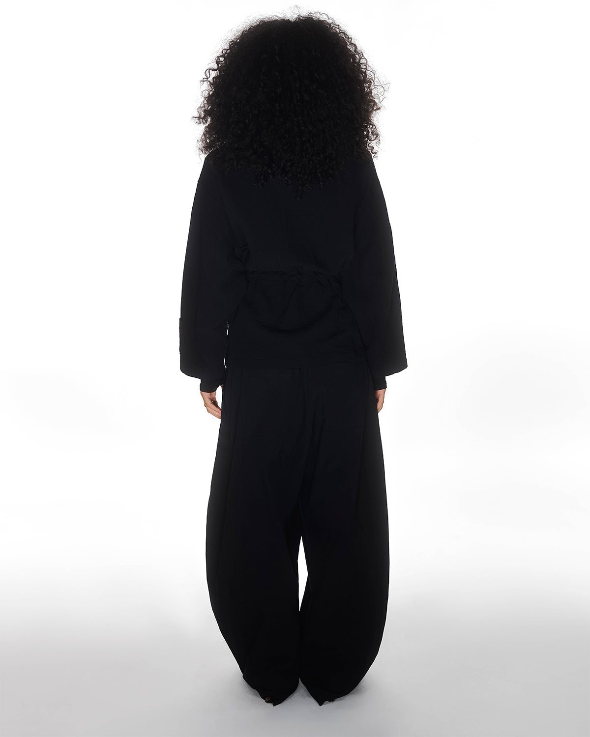 A person with curly hair, facing away from the camera, wears loose-fitting BLACK HANBOK BALLOON PANTS by Sundae School against a white background.