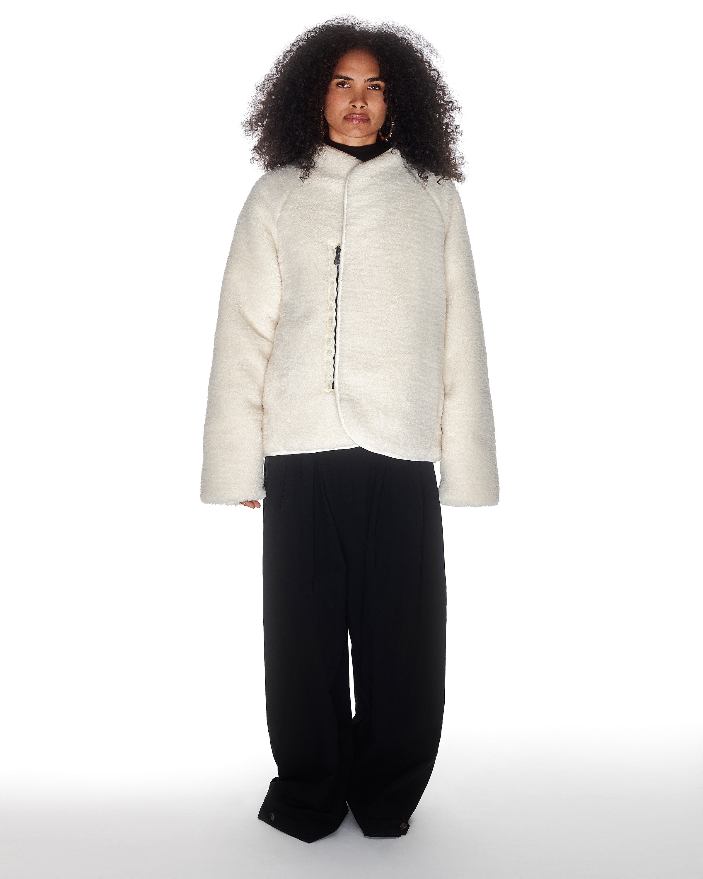 A person with curly hair wears the Sundae School BLACK IVORY REVERSIBLE FLOWER QUILTED JEOGORI FLEECE and loose black pants, standing against a plain white background.