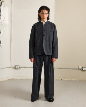 A young person with long dark hair faces forward, wearing Sundae School CHARCOAL PLEATED UNIFORM SLACKS inspired by Korean school uniforms and a dark grey mandarin collar jacket.