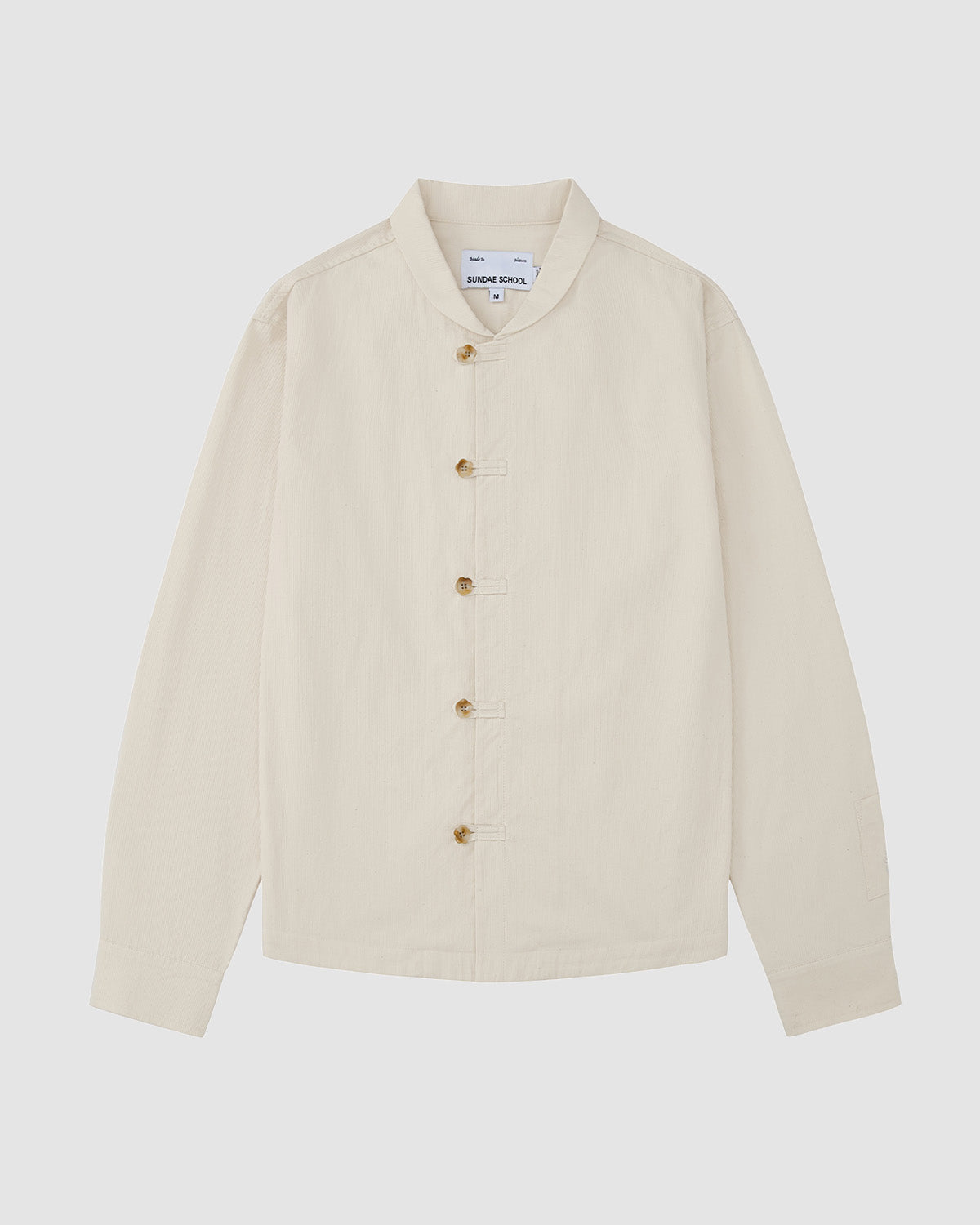 The Sundae School IVORY CHINA COLLAR KNOT SHACKET is a cream, long-sleeve relaxed layer with a mandarin collar and front buttons, made from corded cotton twill and shown laid flat on a light grey background.