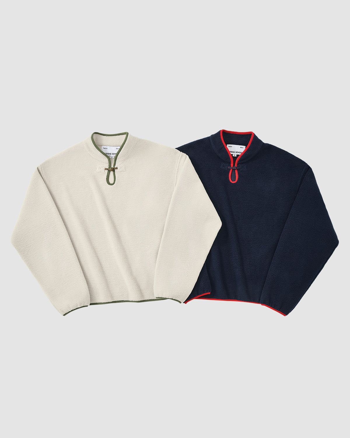 Two TAUPE TEARDROP KNOT FLEECE pullovers by Sundae School are shown: one cream with green trim, one navy with red trim. Both feature a half-zip front, rounded collar, and relaxed fit.
