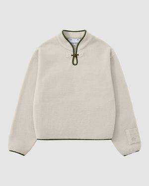 The TAUPE TEARDROP KNOT FLEECE by Sundae School is a cream-colored, long-sleeve pullover with a green-trimmed collar, front toggle closure, green edging on cuffs and hem, and a small patch detail on one sleeve.