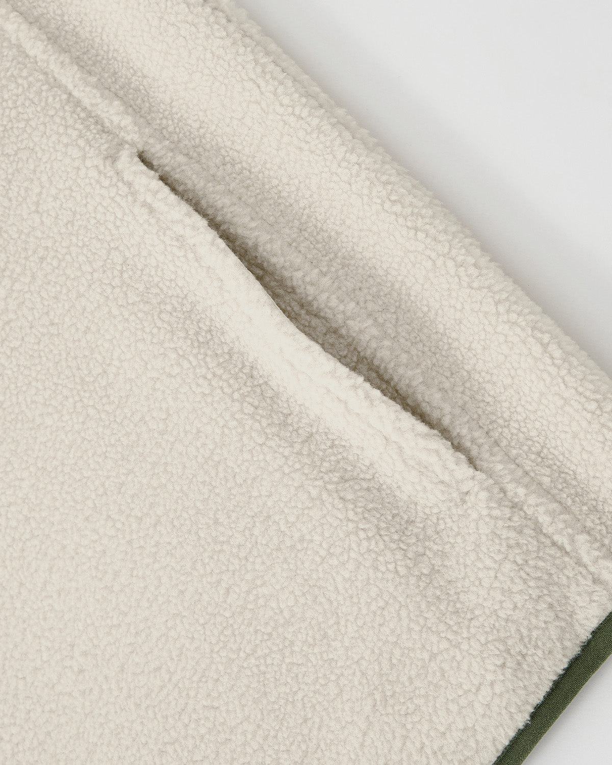 Close-up of the Sundae School TAUPE TEARDROP KNOT FLEECE, highlighting its cream-colored, textured fleece fabric with a slanted side pocket and a small green edge visible at the bottom right.