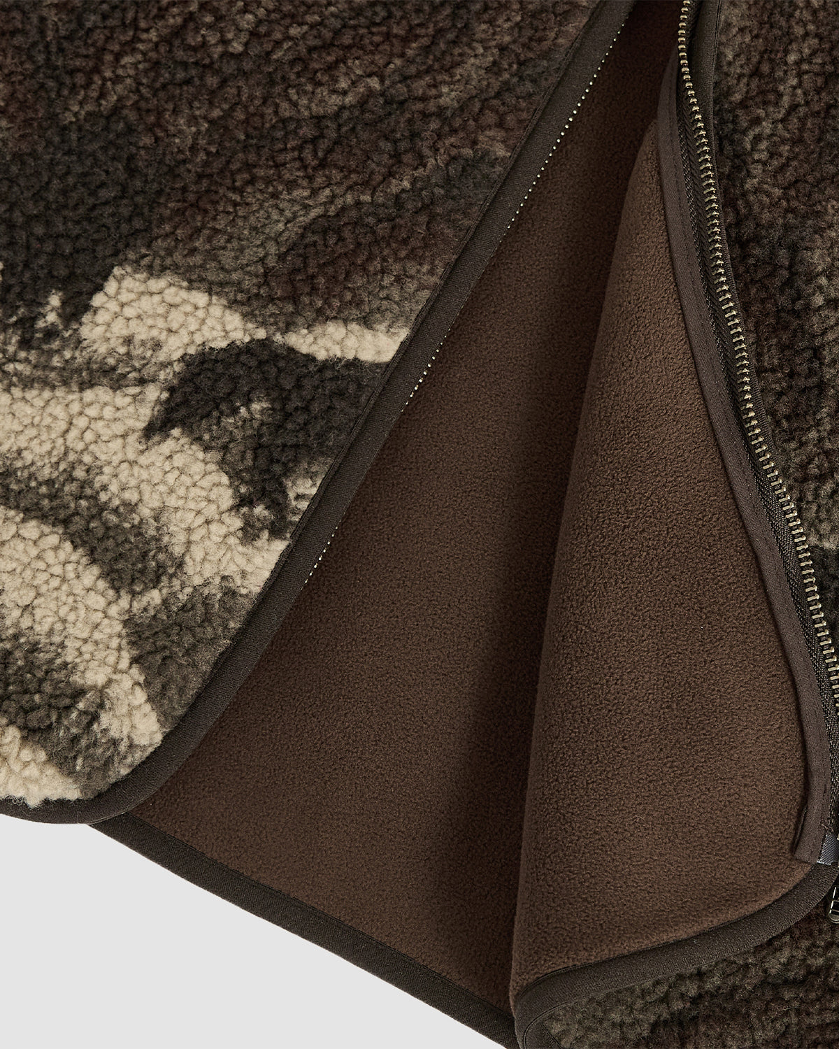 Close-up of the CHARCOAL FIVE PEAKS FLEECE by Sundae School, featuring embossed brown and cream pile fleece, a smooth brown inner lining, and a partially opened zipper along the edge.