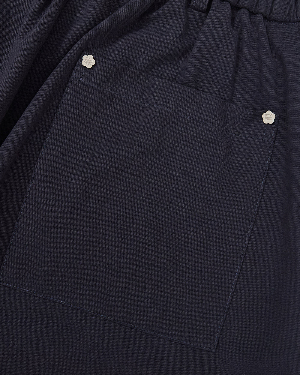 Close-up of the dark blue fabric of the Sundae School NAVY HANBOK BALLOON PANTS, showcasing a large square pocket accented with two small flower-shaped metal studs at the top corners.