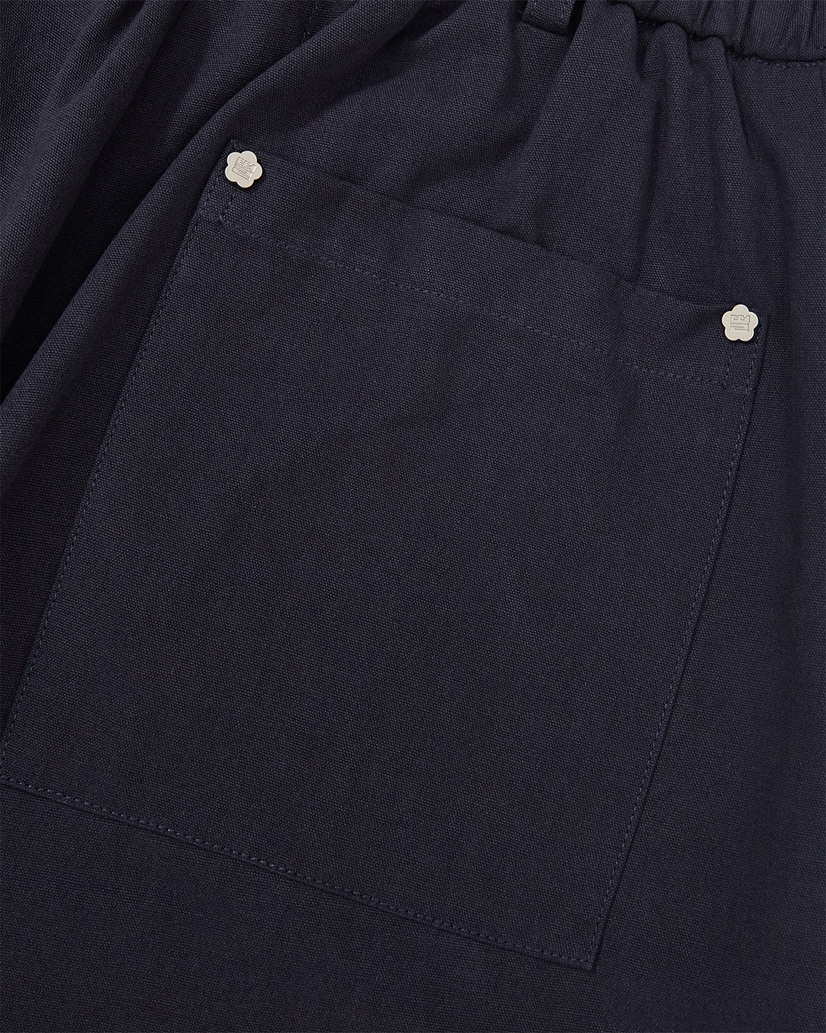 Close-up of the dark blue fabric of the Sundae School NAVY HANBOK BALLOON PANTS, showcasing a large square pocket accented with two small flower-shaped metal studs at the top corners.