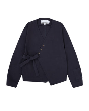 The NAVY HANBOK TIE BLAZER by Sundae School is crafted from 100% cotton in a navy blue hue, featuring a wrap-style silhouette with an asymmetrical front. It is detailed with a fabric belt for side tie closure, four buttons, and a single cuff accent on the sleeve.