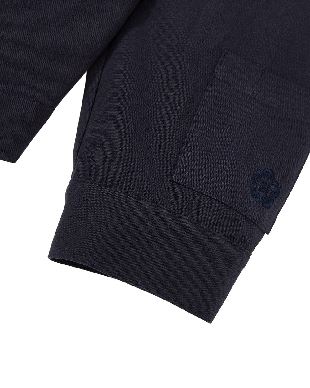 Close-up of the sleeve of the Sundae School NAVY HANBOK TIE BLAZER, featuring a ribbed cuff and a pocket adorned with an embroidered floral or clover-shaped design, all crafted from 100% cotton.