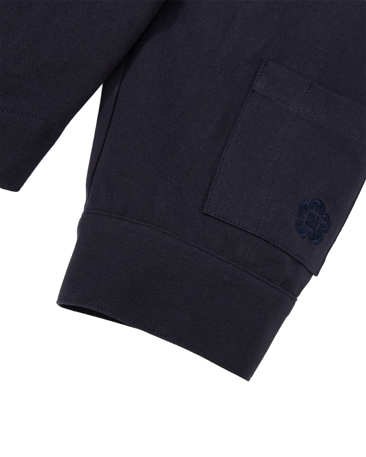 Close-up of the sleeve of the Sundae School NAVY HANBOK TIE BLAZER, featuring a ribbed cuff and a pocket adorned with an embroidered floral or clover-shaped design, all crafted from 100% cotton.