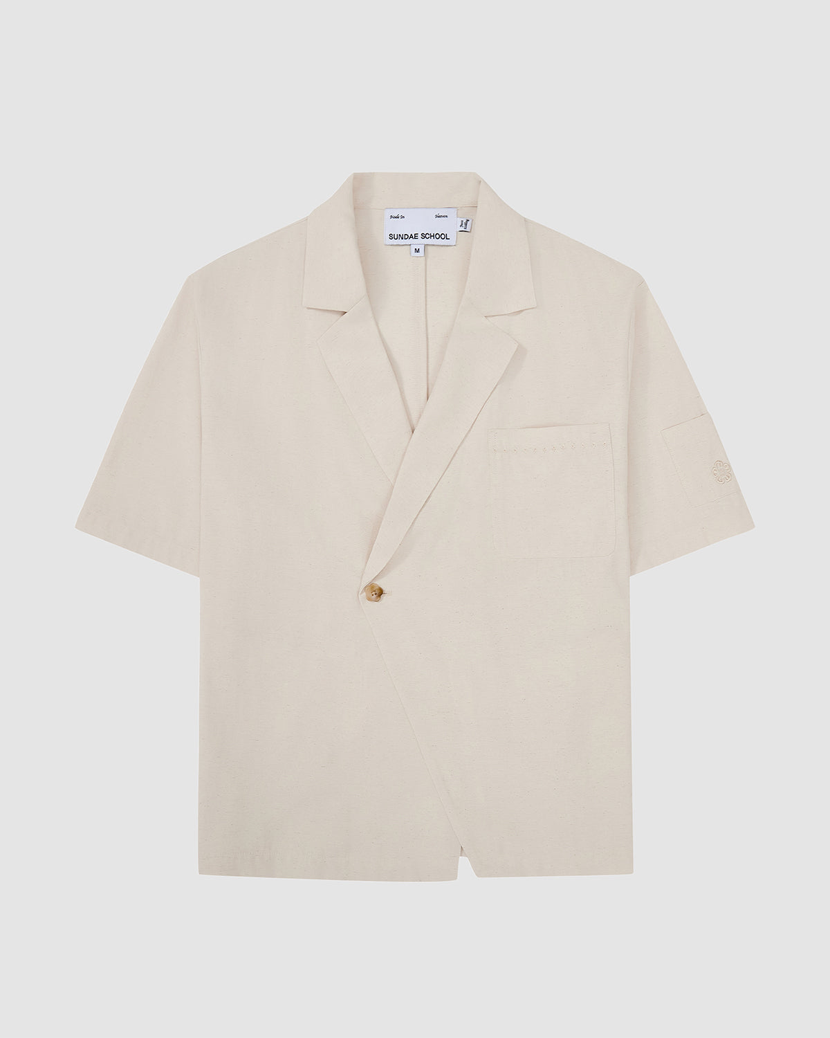 Sundae School cream hanbok-inspired short sleeve shirt with asymmetric wrap front closure, single button fastening, chest pocket, and relaxed fit silhouette, flat lay photography on light gray background