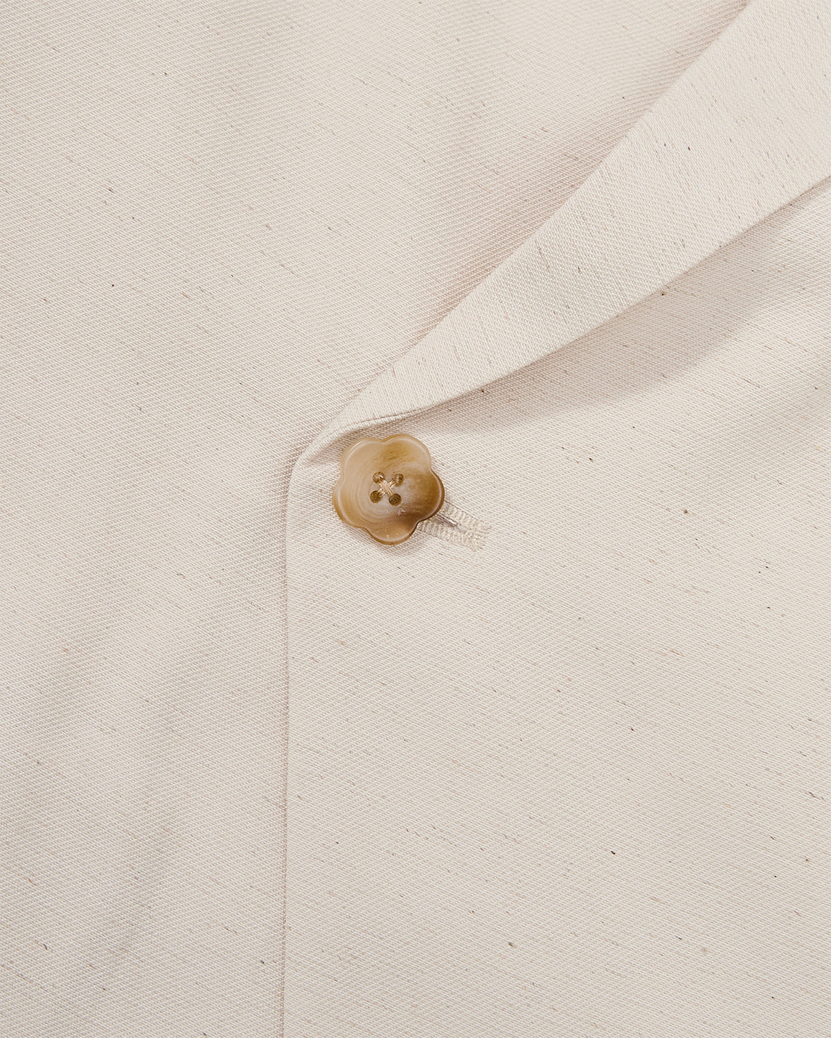 Close-up detail of cream hanbok shirt showing tan flower-shaped button with four holes on lightweight linen fabric, demonstrating asymmetric closure hardware