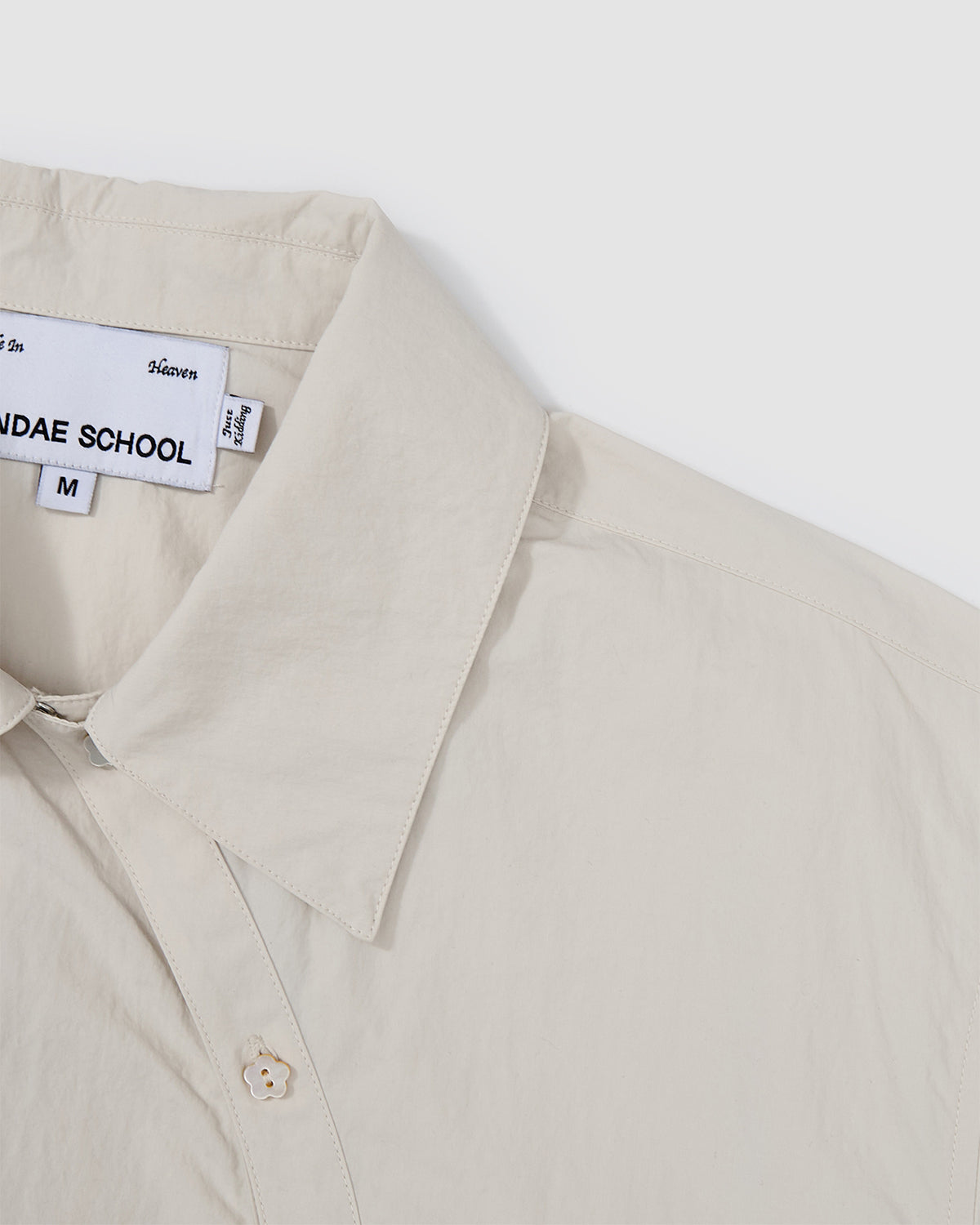 Detail view of the collar and curved button placket construction on the Ivory Yin Yang Short Sleeve Shirt showing the Sundae School brand label.