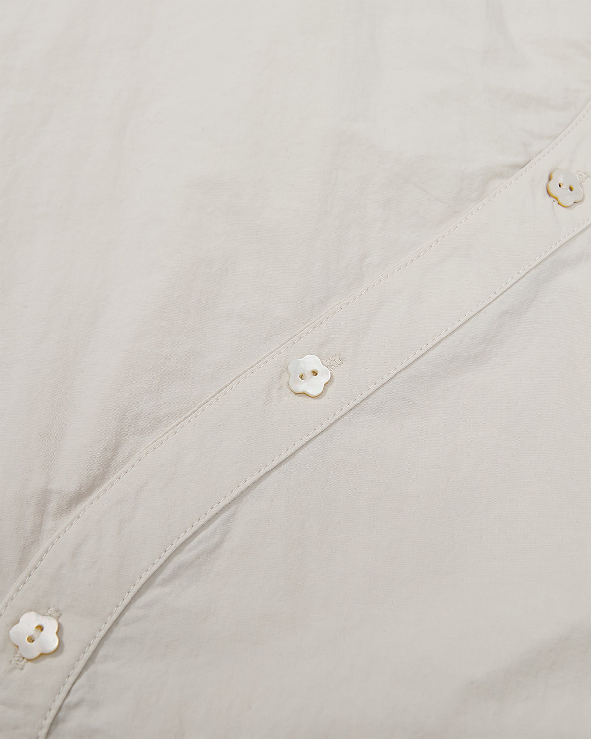 Close-up of white flower-shaped mother-of-pearl buttons along the curved asymmetrical placket of the Ivory Yin Yang Short Sleeve Shirt.