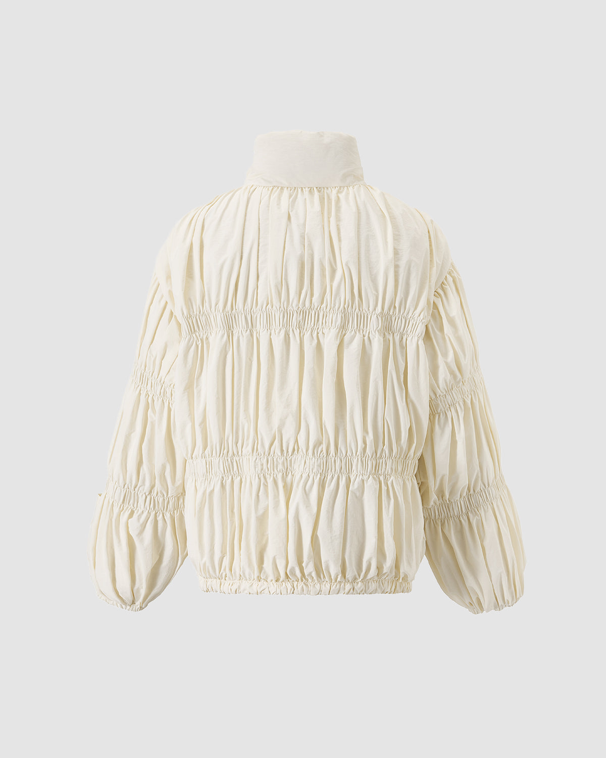 The IVORY PLEATED DUVET PUFFER by Sundae School is a cream-colored, long-sleeved jacket with a high collar and ruched, pleated detailing, displayed against a plain light gray background.