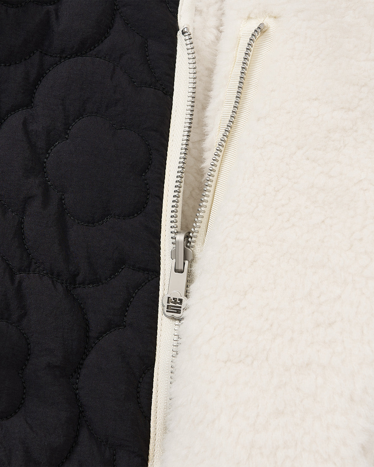 Close-up of Sundae School's BLACK IVORY REVERSIBLE FLOWER QUILTED JEOGORI FLEECE, showcasing a silver zipper, cream teddy sherpa fleece on one side, and black quilted fabric with a floral pattern on the other.