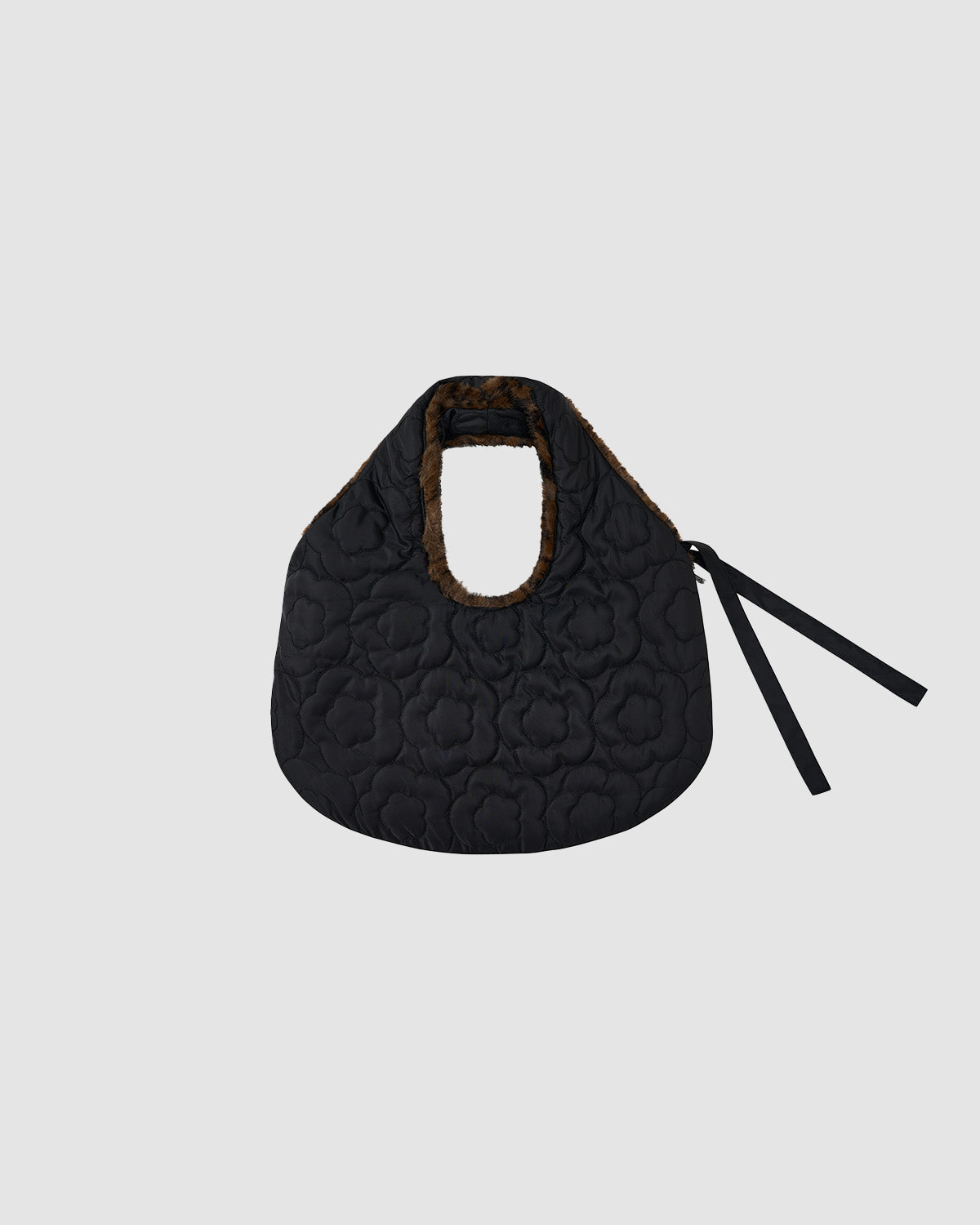 The BLACK LEOPARD BAEJA VEST / BAG by Sundae School is a black, quilted faux fur bag with floral stitching, a rounded shape, brown furry handle, and two long black ribbon ties on the right side, shown on a plain light gray background.