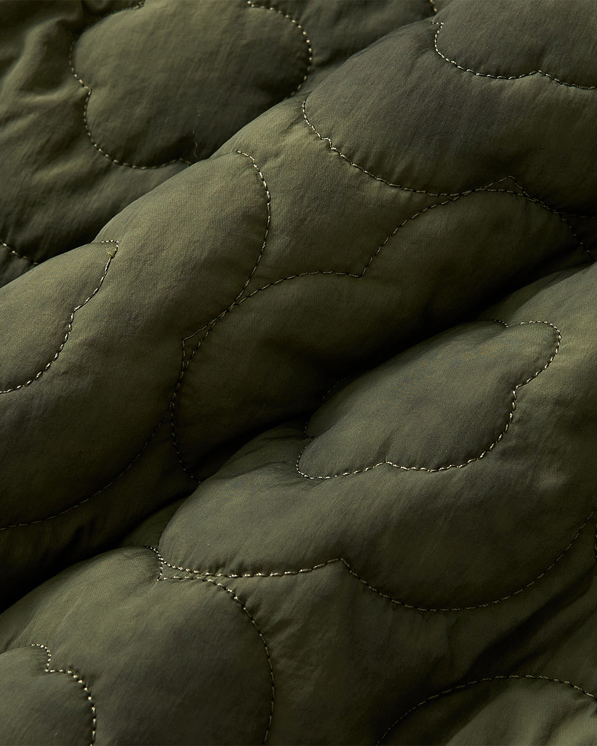 Close-up of Sundae School's MATCHA MOCHI QUILTED MILITARY LINER shows soft, slightly shiny olive green fabric with cloud-like stitching and gentle folds—ideal for a transitional weather jacket.
