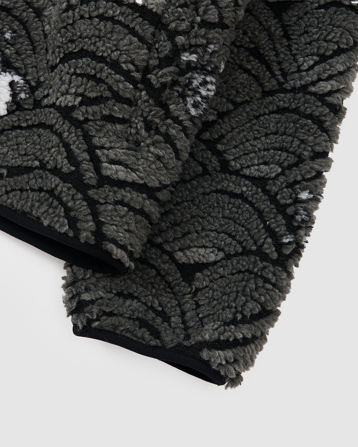 Close-up of Sundae School’s BLACK WAVE FLEECE, showcasing dark gray and black textured fabric with a repeating scallop wave jacquard pattern.