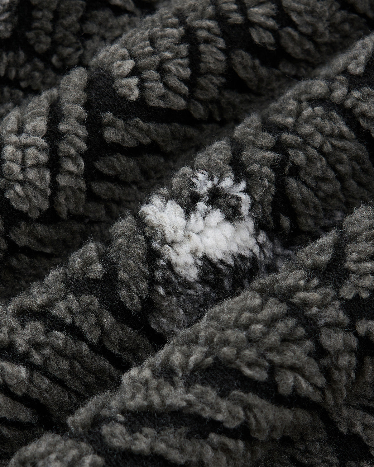 Close-up of Sundae School's BLACK WAVE FLEECE shows its soft, textured dark gray and black fabric, featuring a small white patch in the center that creates a striking, irregular contrast in the pattern.