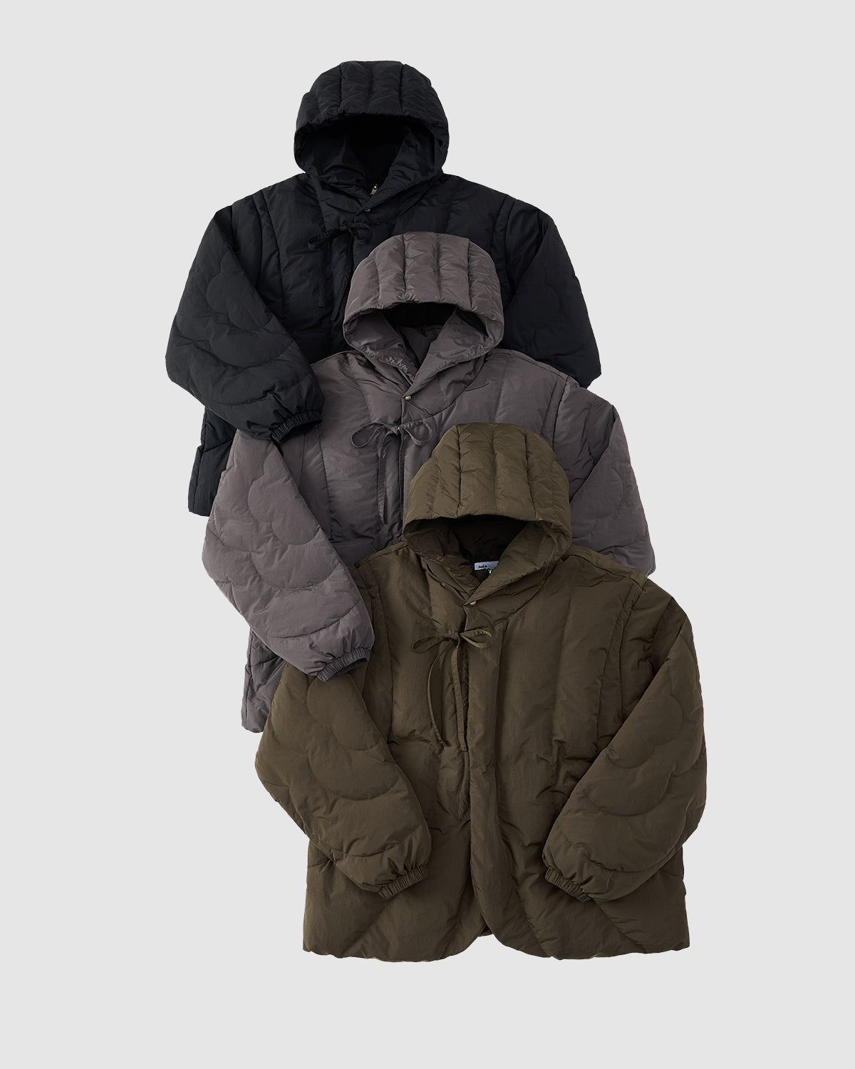 The KHAKI HEAVYWEIGHT MOCHI PUFFER by Sundae School is shown stacked with two other jackets against a light gray background, each displaying subtle Korean hanbok-inspired details.