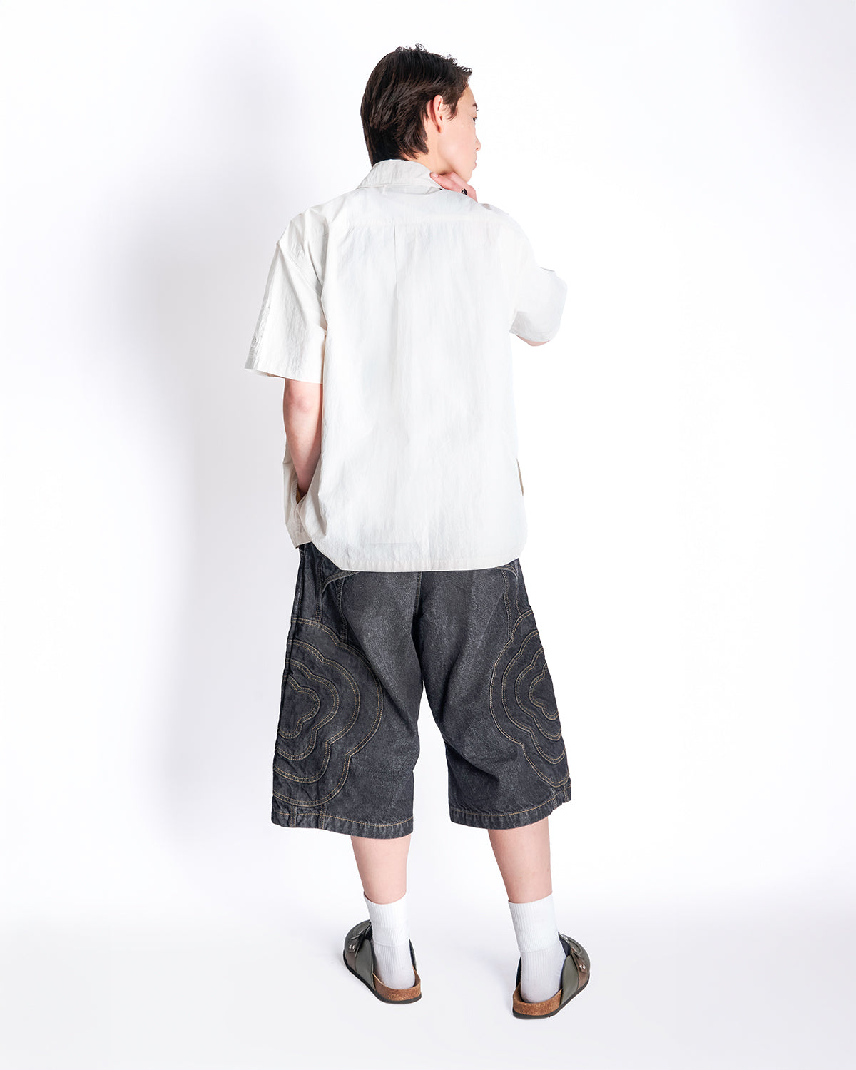 Back view of model wearing the Ivory Yin Yang Short Sleeve Shirt with gray patterned shorts, white socks, and brown sandals.