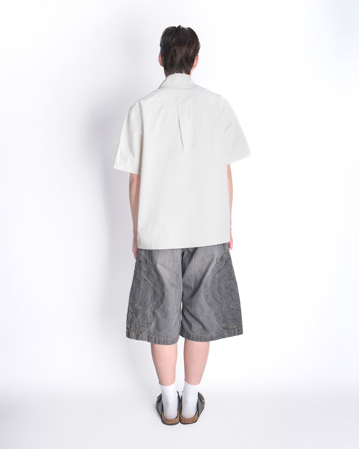 Back view of model wearing the Gray Yin Yang Short Sleeve Shirt with gray patterned shorts, white socks, and brown sandals.