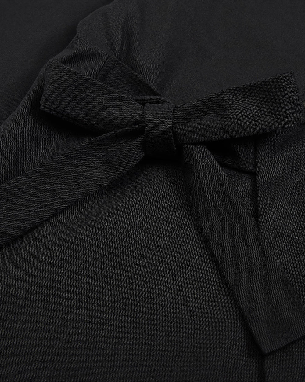 Close-up of the BLACK HANBOK TIE BLAZER by Sundae School, featuring smooth matte black fabric with a neatly tied, slightly off-center bow that recalls the side tie closure and graceful lines of a traditional hanbok jeogori silhouette.