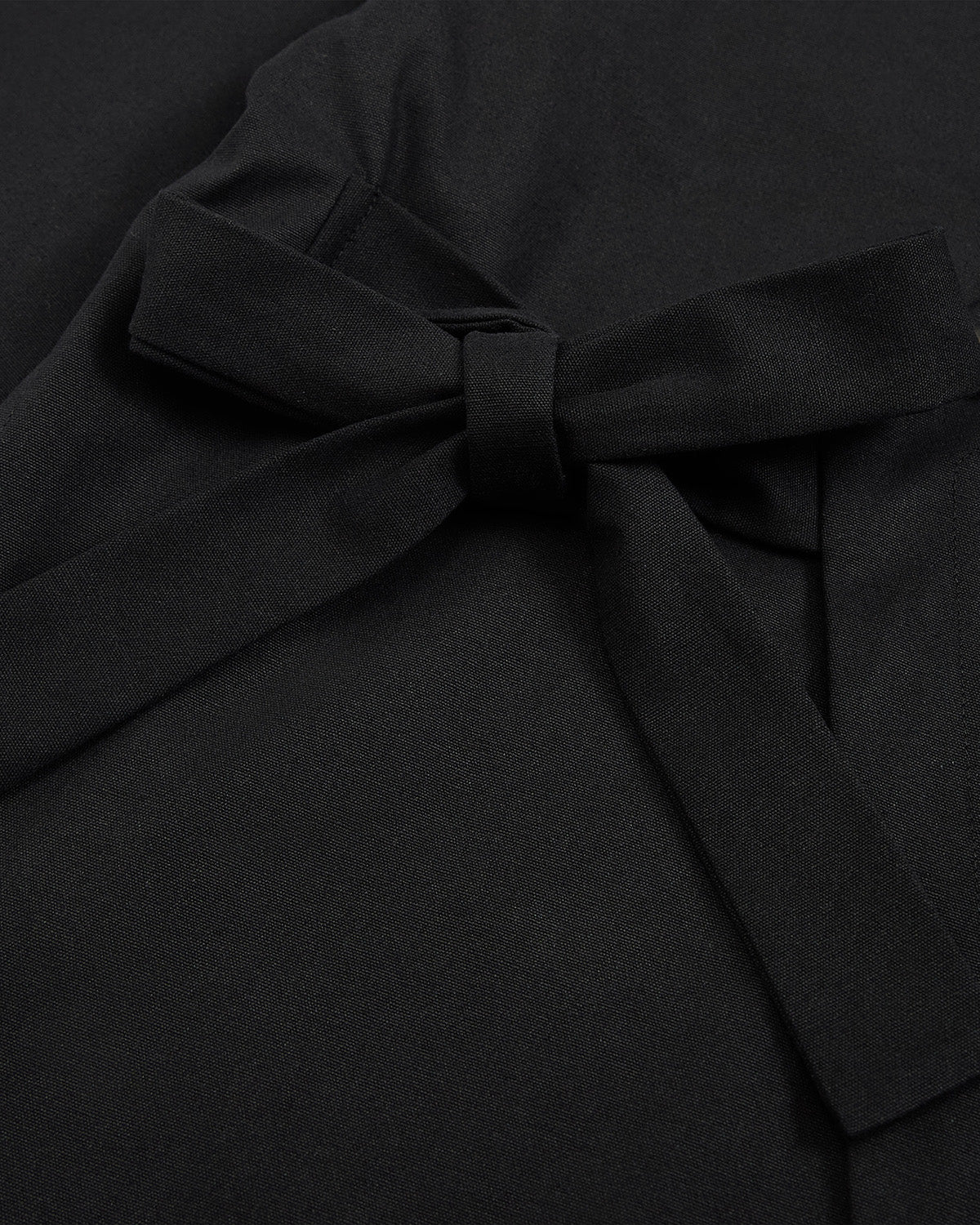 Close-up of the BLACK HANBOK TIE BLAZER by Sundae School, featuring smooth matte black fabric with a neatly tied, slightly off-center bow that recalls the side tie closure and graceful lines of a traditional hanbok jeogori silhouette.