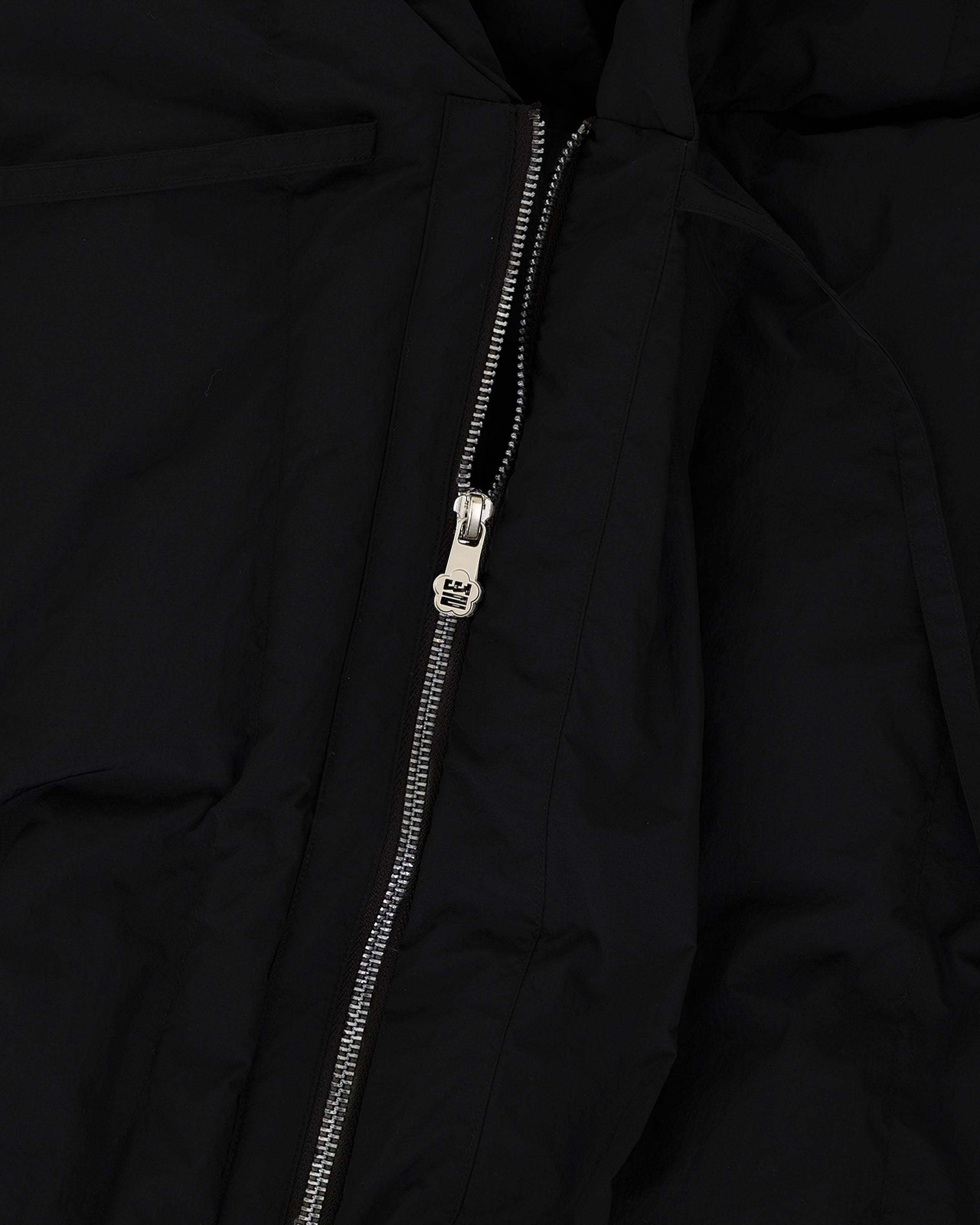 Close-up of a silver zipper partially unzipped on wrinkled black fabric from the BLACK HEAVYWEIGHT MOCHI PUFFER by Sundae School, with the zipper pull centered in the image.